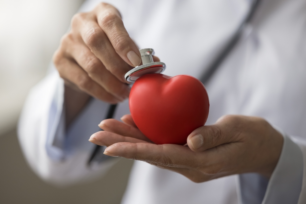 Hands of female cardiologist applying stethoscope to red heart shaped object