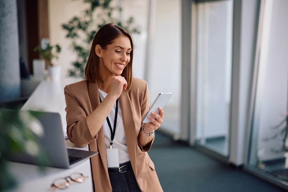 Happy female entrepreneur using smart phone while working in the office. Copy space.